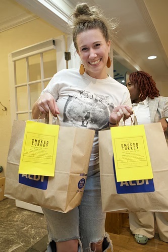 A smiling volunteer holding two bags of smoked turkey ready for pickup